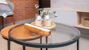 A round glass table with a wooden tray and candles, set against a brick wall and a white cabinet. - Modern 2BR Apt with Balcony Free Parking B53 (Asunción)