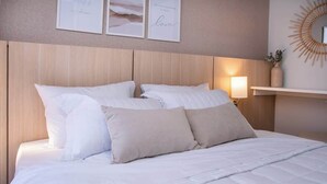 A neatly made bed with white bedding and beige pillows, a wall-mounted mirror, and framed artwork above the bed. - Modern 2BR Apt with Balcony Free Parking B53 (Asunción)