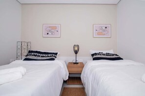 A room with two beds, a nightstand, a lamp, and two framed abstract artworks on the wall. - Cityscape Views - New 2BR Retreat (Asunción)