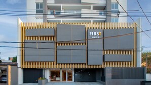 En modern byggnad med en framträdande skylt som visar texten ”FIRST LIVING”, kännetecknad av en slät fasad med stora fönster och en minimalistisk design.