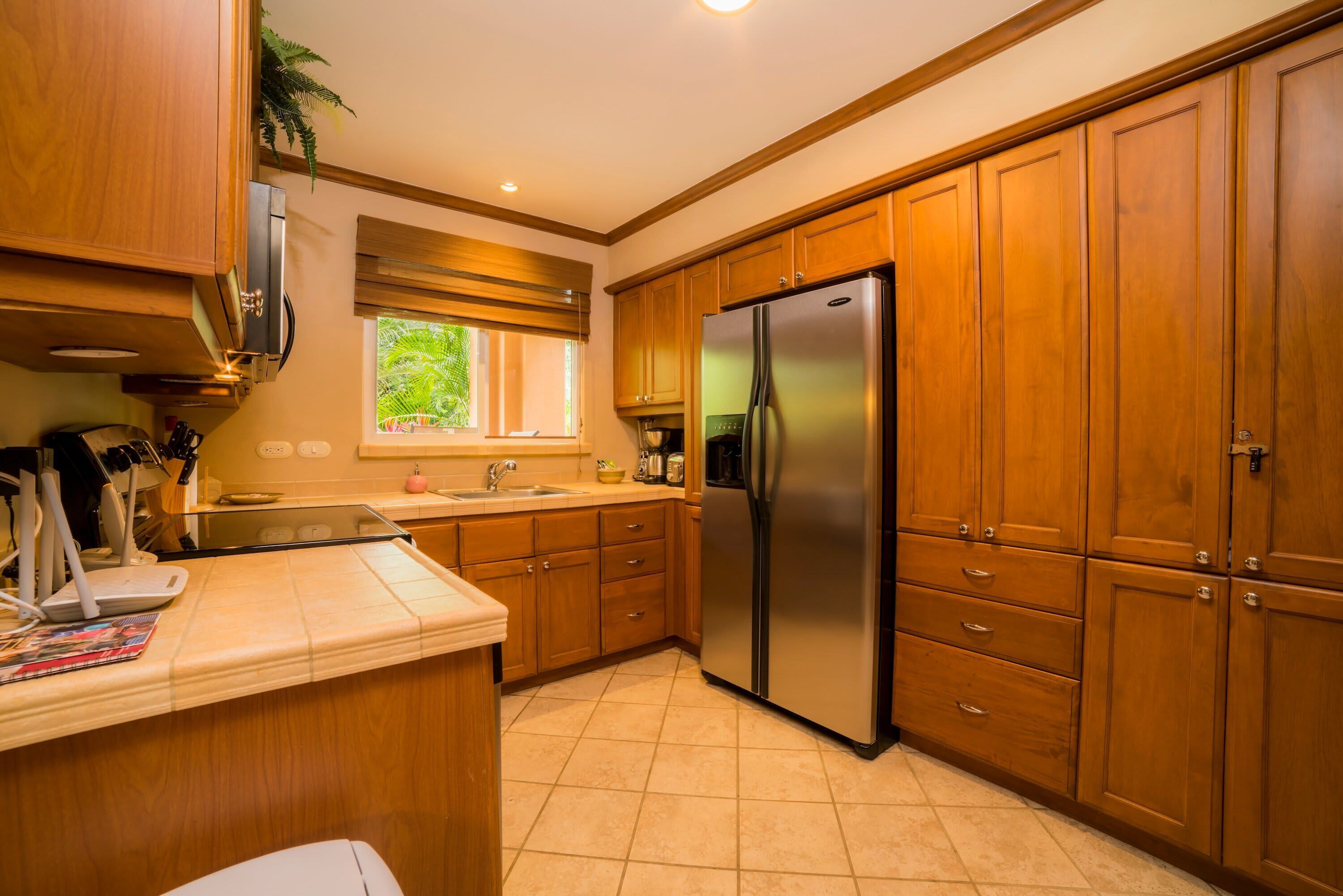 A kitchen with wooden cabinets, a stainless steel refrigerator, and a window with blinds.