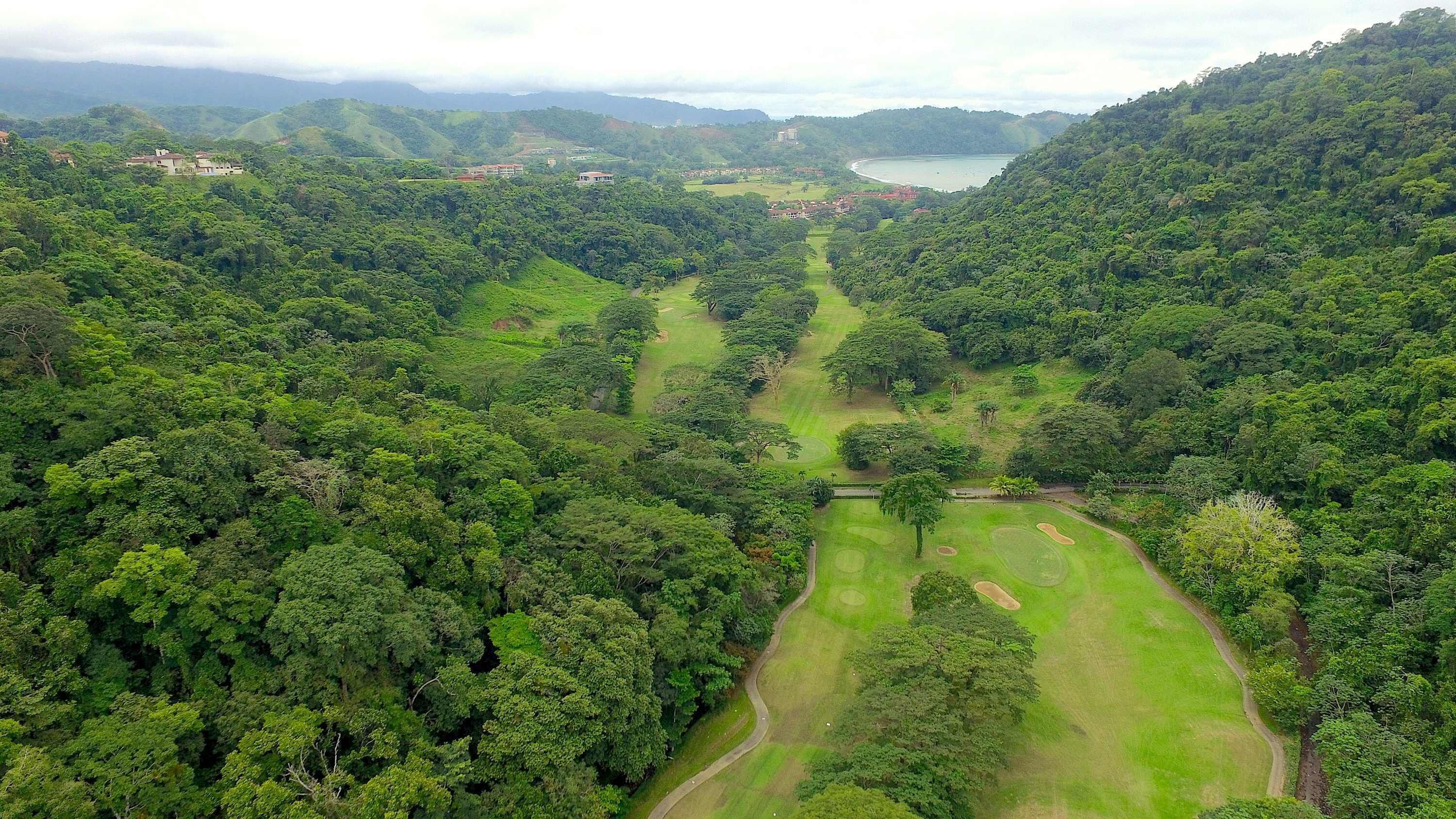 Üppige grüne Landschaft mit einem Golfplatz, umgeben von dichtem Wald und Hügeln.