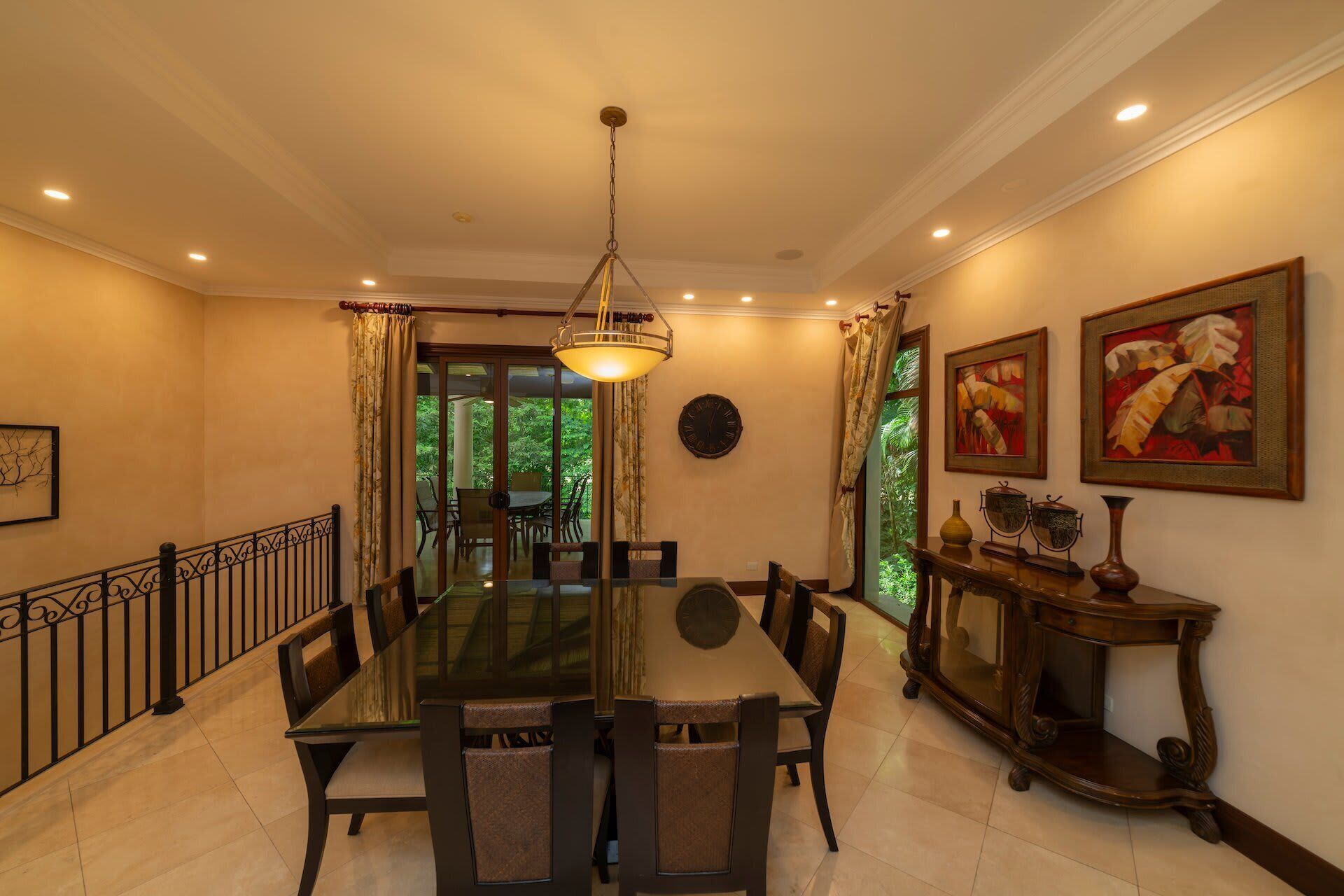 A dining area with a glass-top table, chairs, a chandelier, and artwork on the walls.