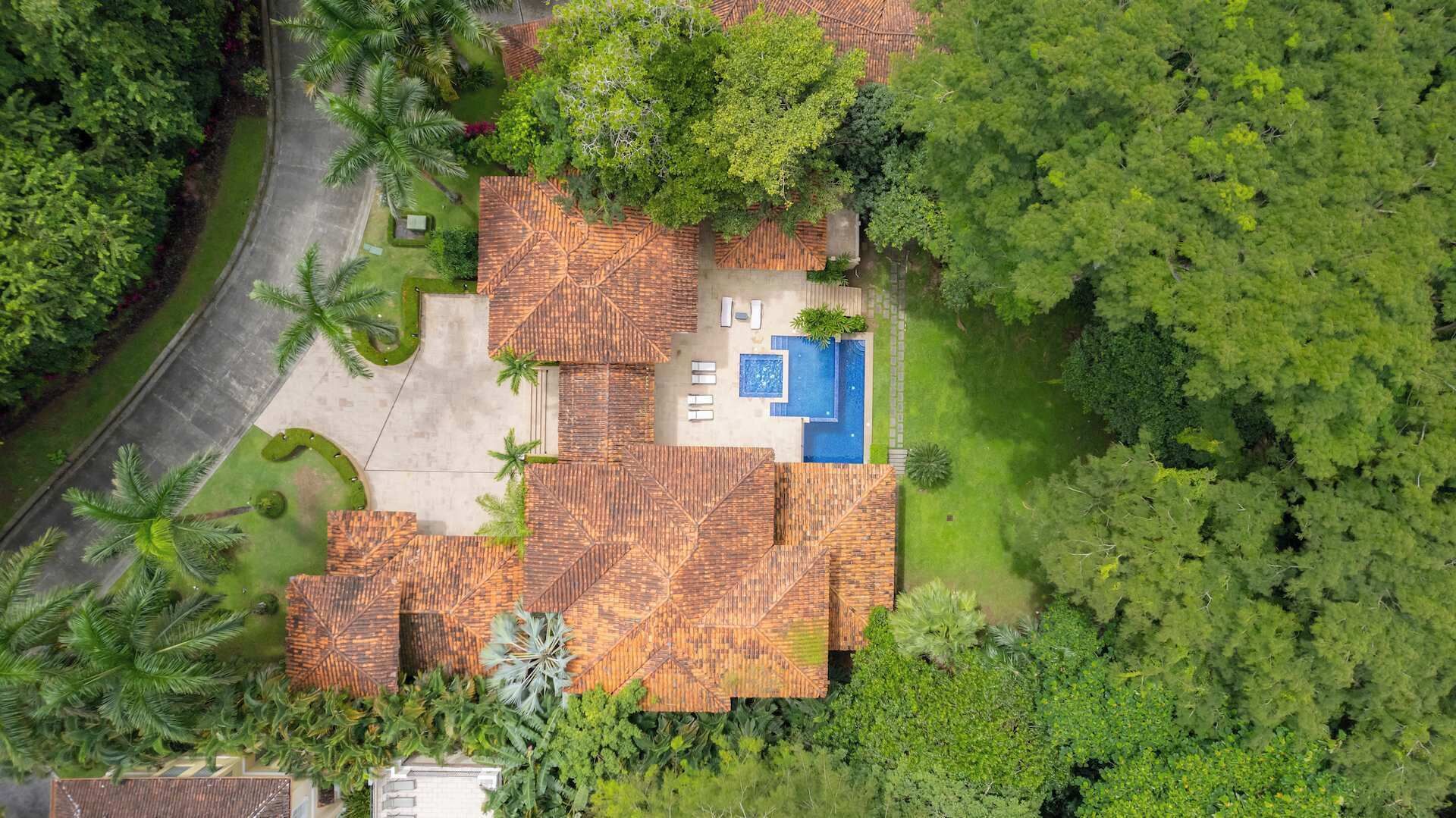 An aerial view of a property with a central swimming pool, multiple rooms with sloped roofs, and surrounding greenery.