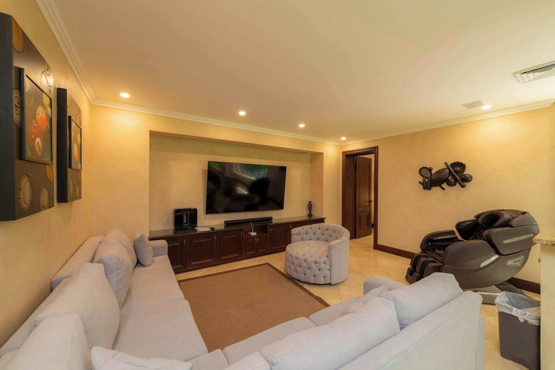 A living room with a large flat-screen TV, a sofa, a round ottoman, and exercise equipment.