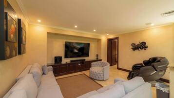A living room with a large flat-screen TV, a sofa, a round ottoman, and exercise equipment.
