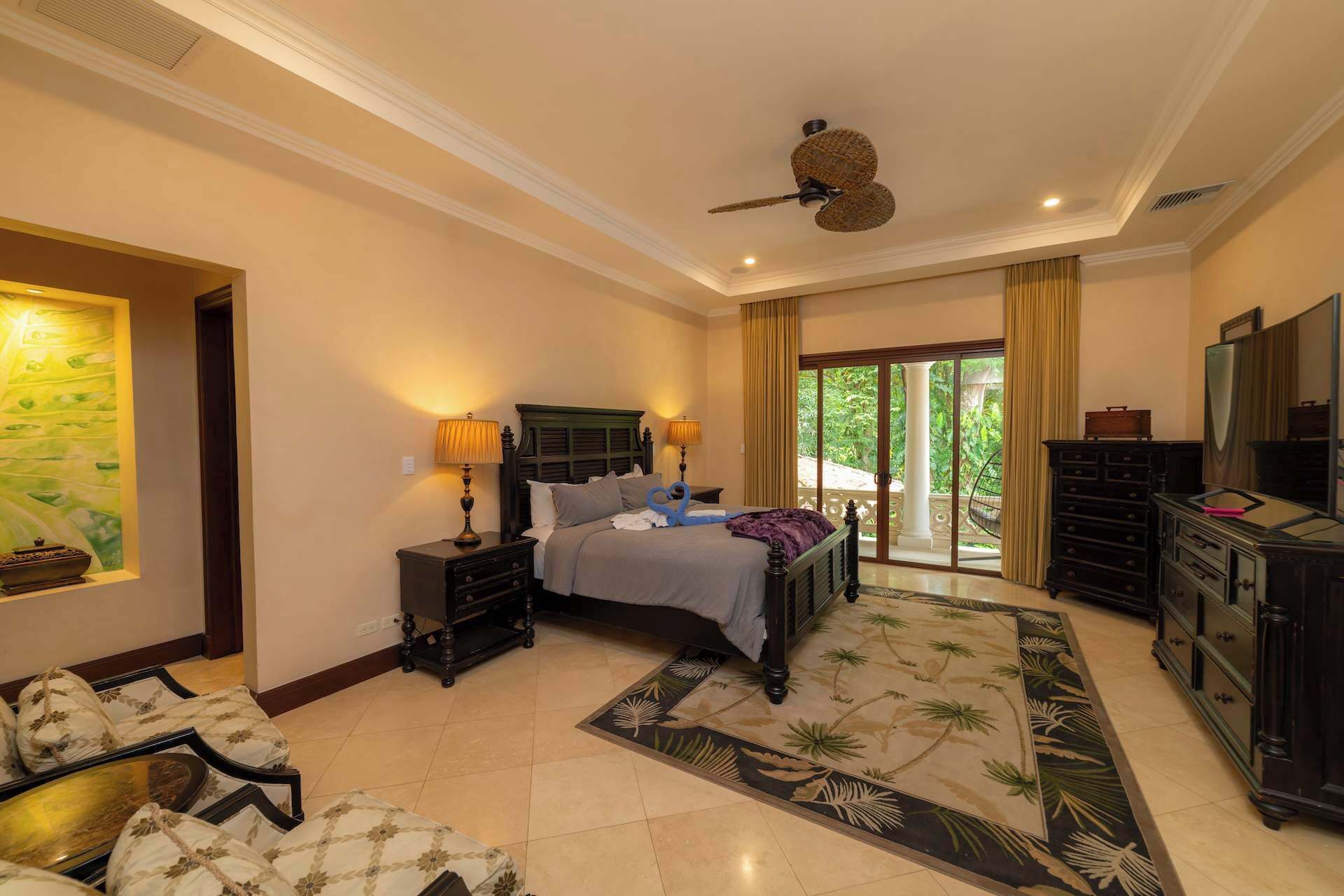 A hotel room with a bed, nightstands, a dresser, a television, and a view of the outdoors.