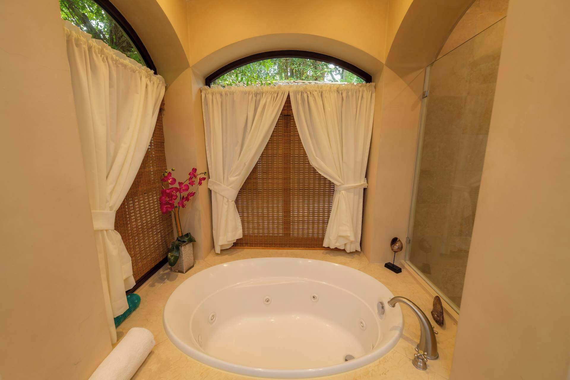 A bathroom with a large bathtub, a shower, and a window with curtains.