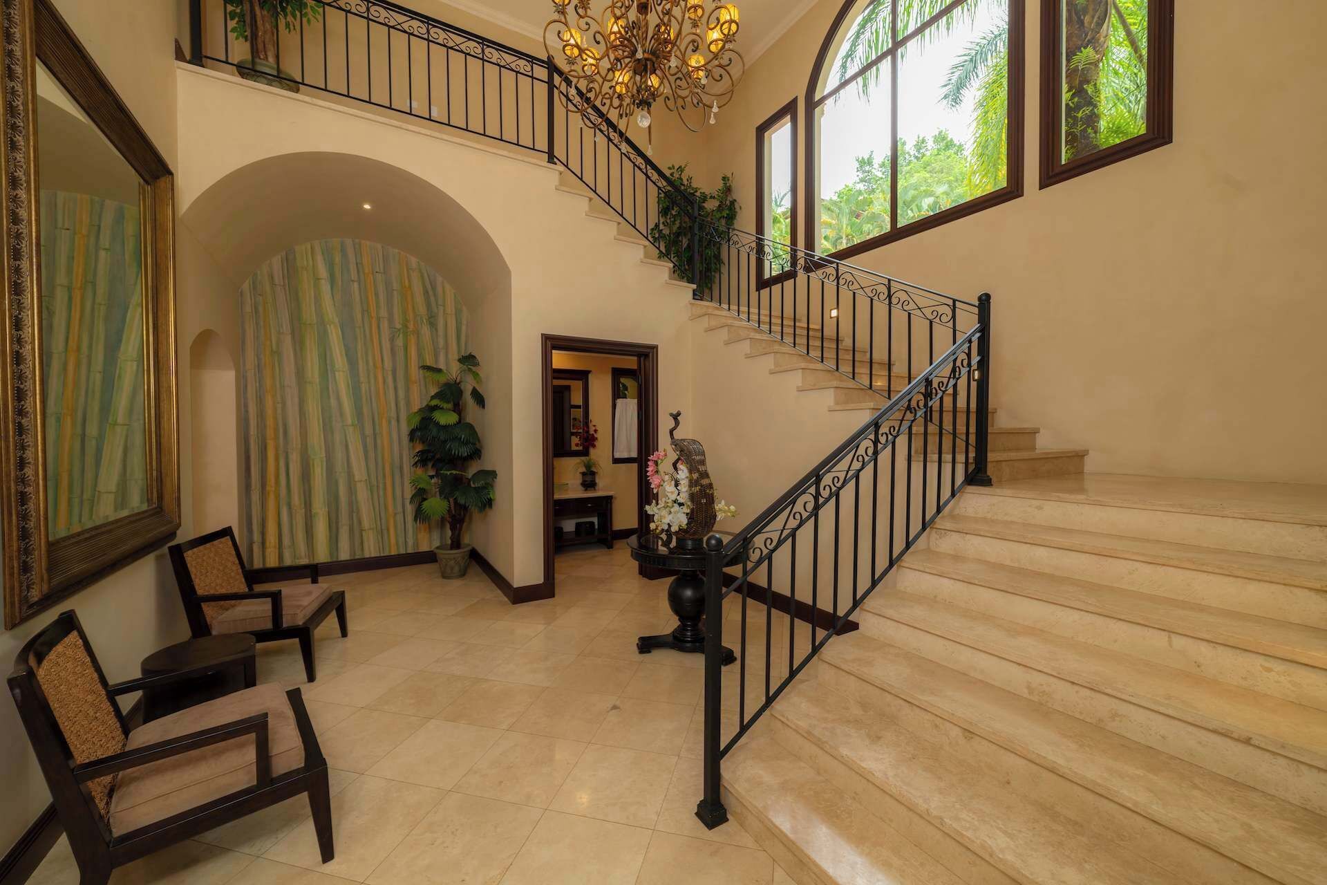 A spacious foyer with a grand staircase, a seating area with chairs, and a large window with a view of greenery.