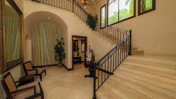 A spacious foyer with a grand staircase, a seating area with chairs, and a large window with a view of greenery.
