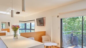 A modern interior with a white reception desk, a vase of flowers, a seating area with a sofa and chairs, and a balcony with a metal railing. - Beautiful Studio with Botanical Garden Views (Buenos Aires)