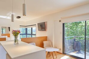 A modern interior with a white reception desk, a vase of flowers, a seating area with a sofa and chairs, and a balcony with a metal railing. - Beautiful Studio with Botanical Garden Views (Buenos Aires)