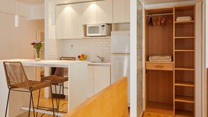 A compact kitchen with white cabinets, a microwave, and a small island with stools. - Beautiful Studio with Botanical Garden Views (Buenos Aires)