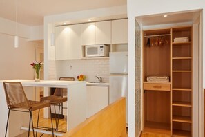 A compact kitchen with white cabinets, a microwave, and a small island with stools. - Beautiful Studio with Botanical Garden Views (Buenos Aires)