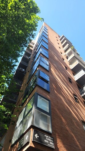 A tall brick building with multiple floors, large windows, and a sign indicating 'Juan María Gutiérrez 4000 - 3900, Comuna 14.' - Beautiful Studio with Botanical Garden Views (Buenos Aires)