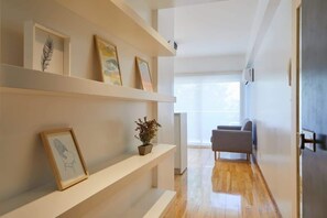 A hallway with white shelves displaying framed artwork, a potted plant, and a gray chair. - Beautiful Studio with Botanical Garden Views (Buenos Aires)
