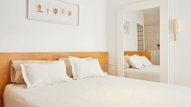 A hotel room with a bed, a headboard, a bedside table, a mirror, and a framed picture on the wall. - Beautiful Studio with Botanical Garden Views (Buenos Aires)