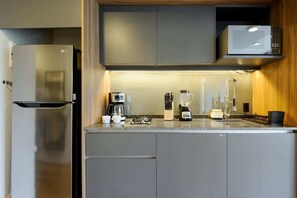Eine kleine Küche mit Kühlschrank, Mikrowelle, Kaffeemaschine und Mixer auf der Arbeitsfläche.