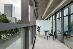 Ein moderner Balkon mit Glasgeländern, einem Blumentopf und einem kleinen Tisch mit Stühlen.