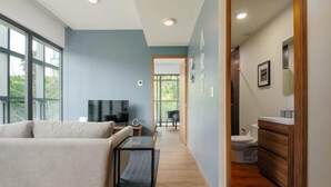 A modern living room with a sofa, a coffee table, and a TV. There is a hallway leading to a bathroom with a toilet and a sink. - Furnished 1 Bedroom Apartment in Mexico City (Ciudad de México)