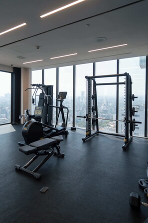 Ein Fitnessraum mit Trainingsgeräten und Blick auf die Stadt durch große Fenster.
