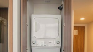 A compact laundry room with a front-loading washer and dryer, wooden flooring, and a door leading to another room. - Furnished 2 Bedroom Apartment in Mexico City (Ciudad de México)