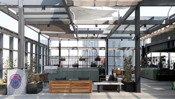 An outdoor seating area with wooden benches and tables, surrounded by planters and a large window offering views of the city. - Furnished 2 Bedroom Apartment in Mexico City (Ciudad de México)