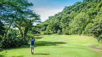 Un campo de golf con un paisaje verde exuberante, cielo despejado y un fondo montañoso.