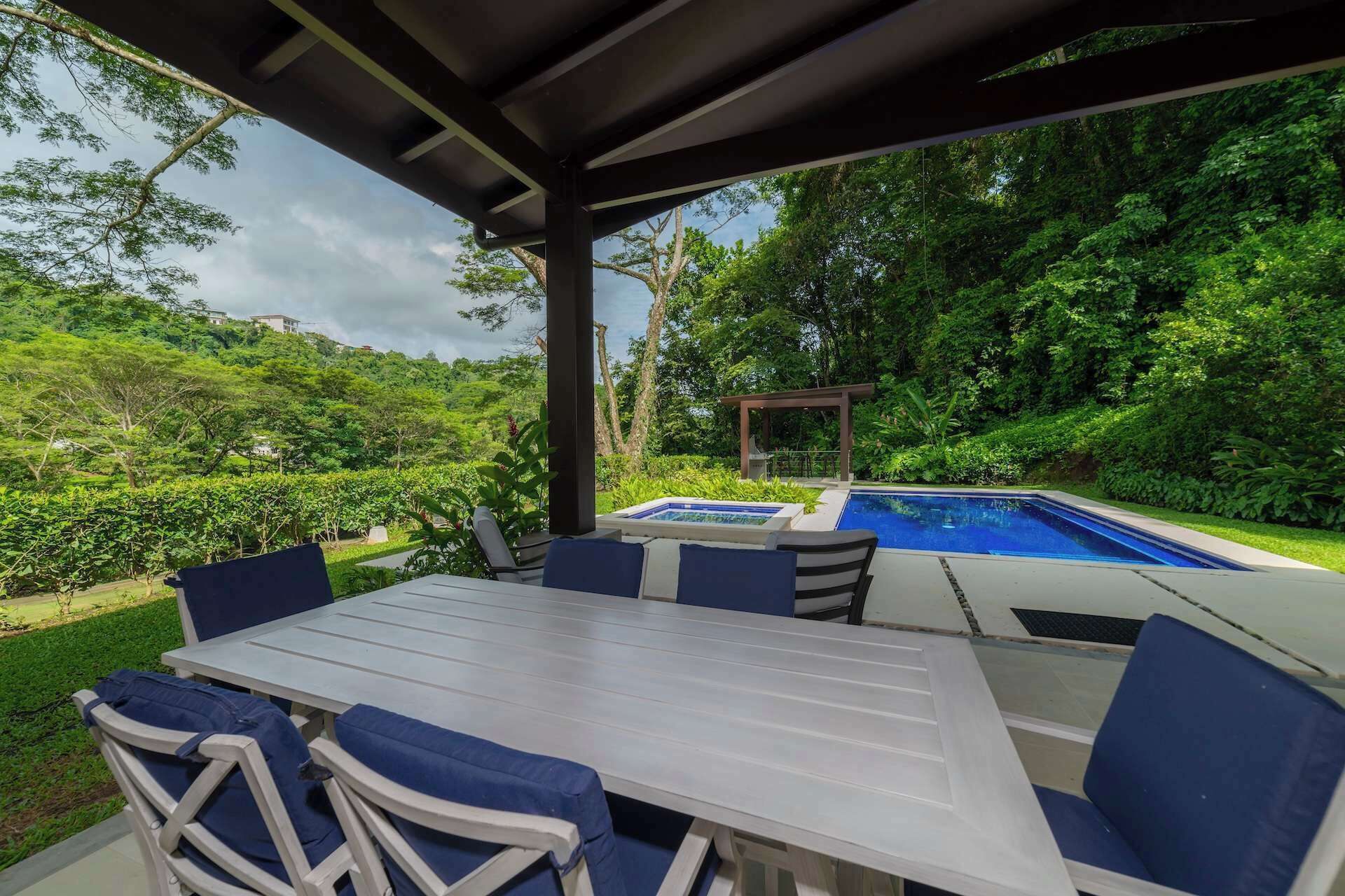 An outdoor patio with a pool, surrounded by lush greenery and a pergola.