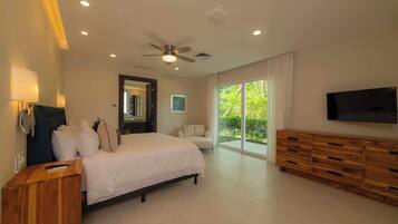 A bedroom with a bed, a vanity, a ceiling fan, a TV, and a large window.