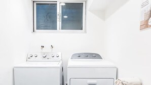 Ein Waschraum mit zwei Waschmaschinen, einem Trockner, einem Fenster und einem Tisch mit gefalteten Handtüchern.
