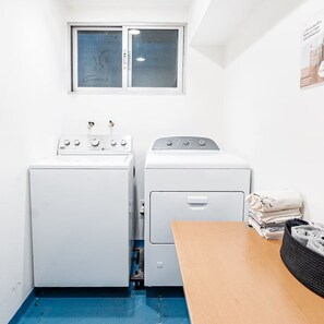 A laundry room with two washing machines, a drying machine, a window, and a table with folded towels. - Top Bed | Mixed Shared Room (Ciudad de México)