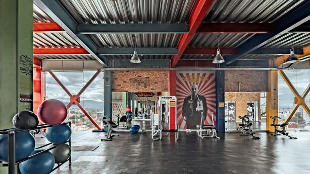 Ein Fitnessstudio mit unterschiedlichen Trainingsgeräten, einem großen Wandgemälde und Blick auf die Stadt.