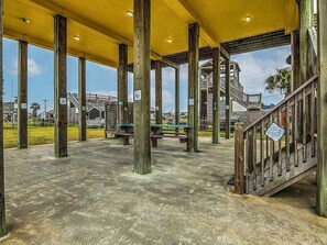 A covered outdoor area with wooden pillars, a concrete floor, and a staircase leading to a higher level. - Sarenity - 3Bd 2Bth, 8 Guests, Pet Friendly (Bolivar Peninsula)