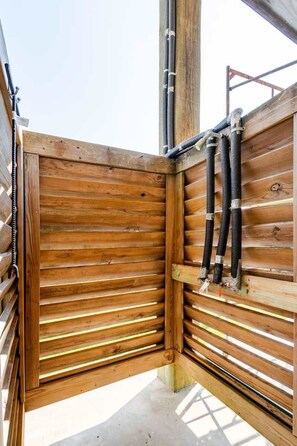 A corner of a wooden structure with horizontal slats, metal pipes, and a concrete floor. - Sarenity - 3Bd 2Bth, 8 Guests, Pet Friendly (Bolivar Peninsula)