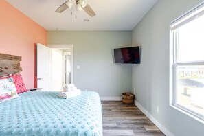 Ein Schlafzimmer mit Bett, Deckenventilator, Fernseher, Fenster und Tür.