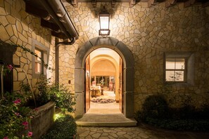 Fachada de piedra con una entrada abovedada, un farol y vistas al interior iluminado.