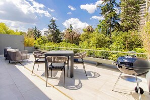 Eine Terrasse im Freien mit Tisch, Stühlen, einem Grill und Blick auf Bäume und Gebäude.
