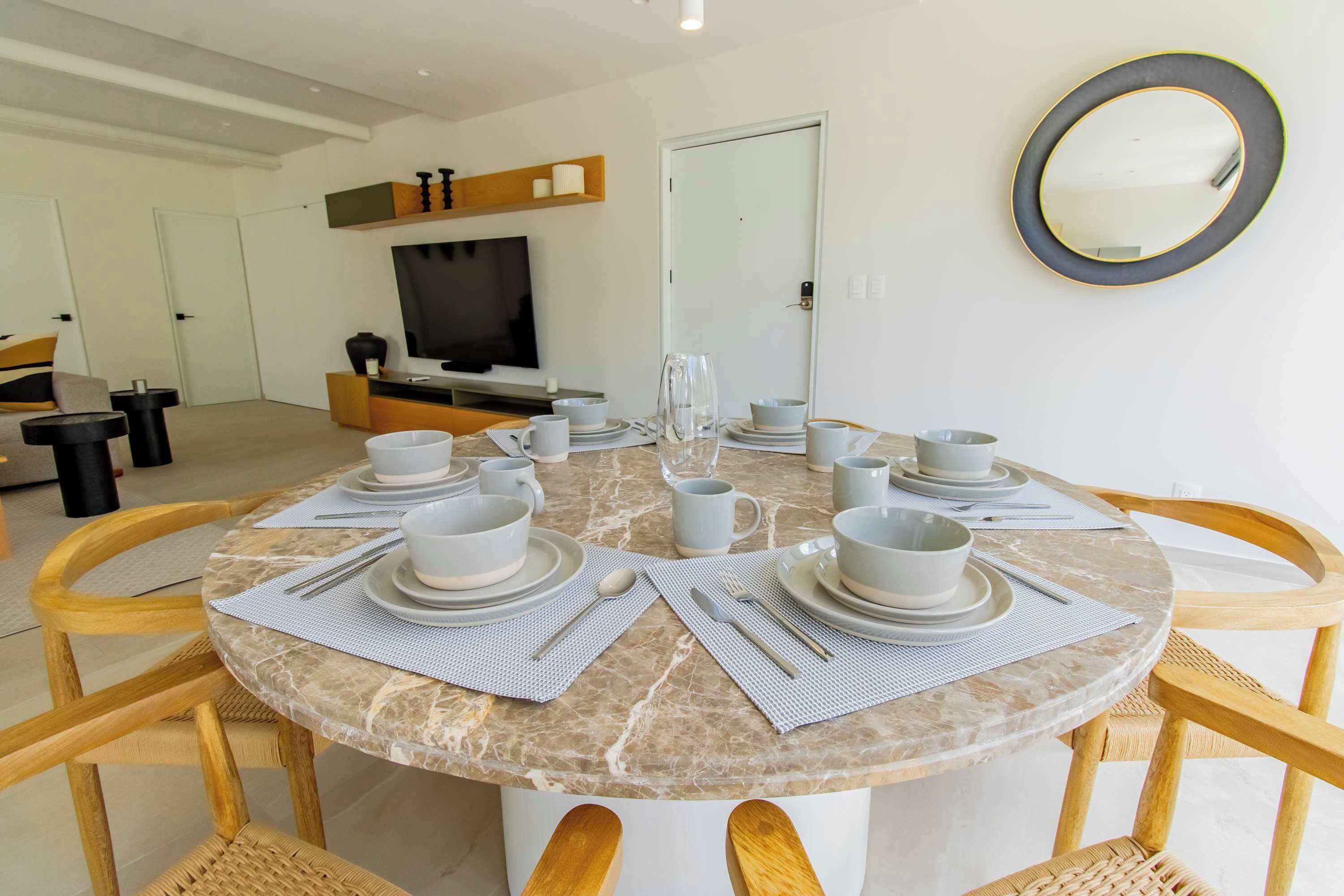 A dining area with a round table set for six, surrounded by wooden chairs.