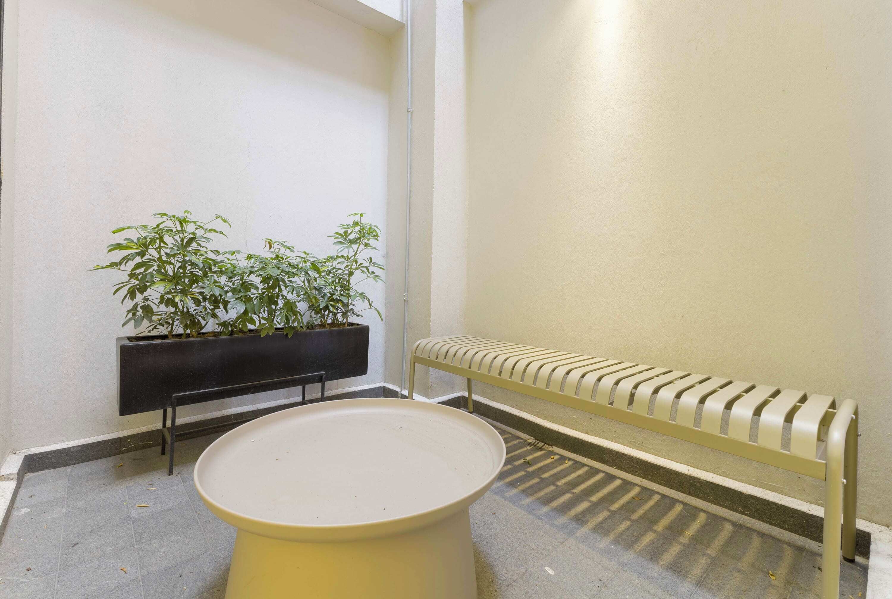Un espacio pequeño y cerrado con un banco, una maceta con plantas verdes y una mesa redonda.
