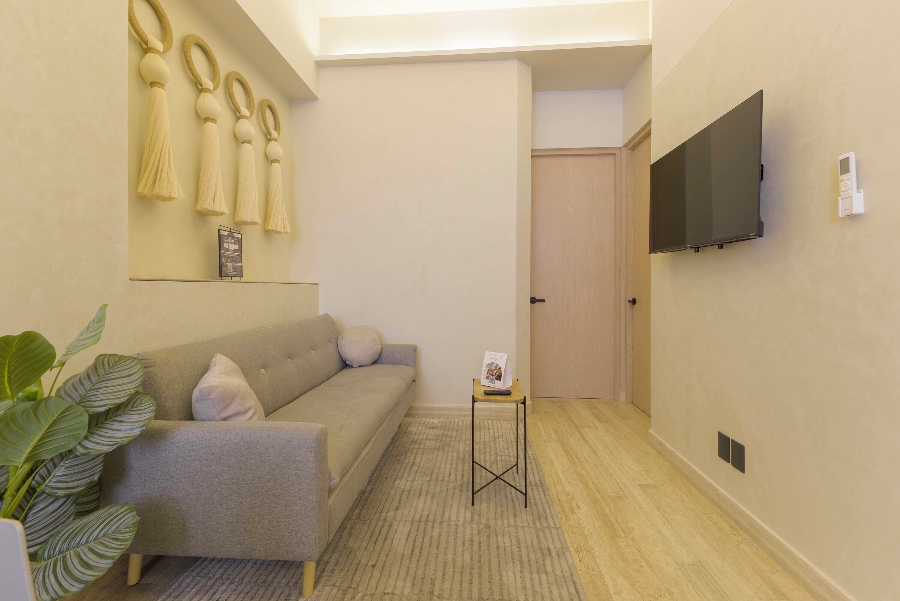A modern living room with a grey sofa, a small table with a remote, and a TV mounted on the wall.