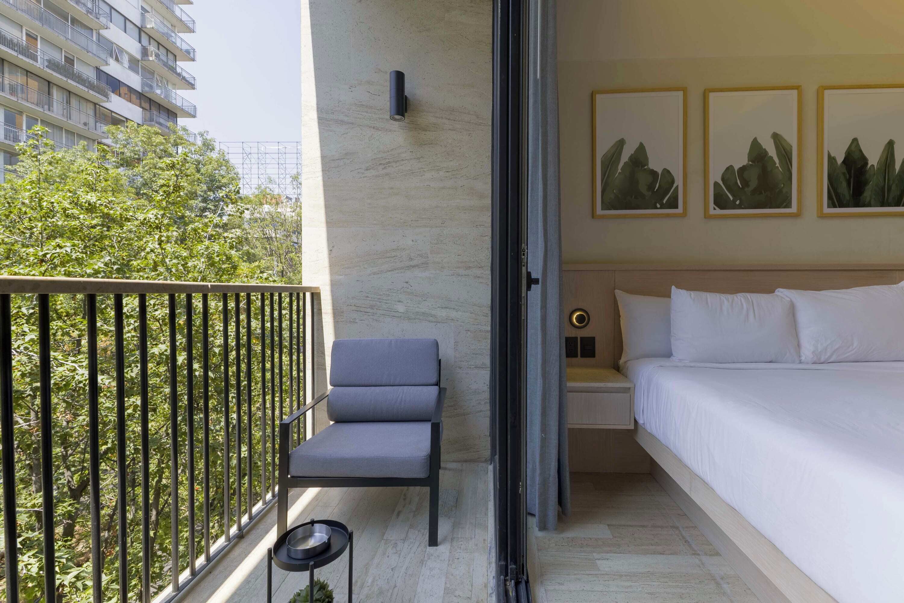 Ein modernes Hotelzimmer mit Balkon, einem Bett, einem Sessel und Bildern an der Wand.