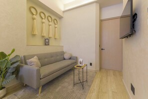 Ein stilvolles Zimmer mit einer Couch, einem kleinen Tisch, einer Topfpflanze und einem an der Wand befestigten Fernseher.