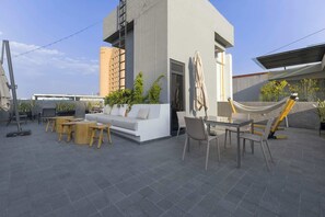 Een terras op het dak, met een bank, eettafel, stoelen, een hangmat en potplanten.