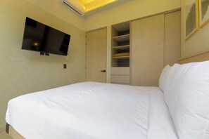 Ein Hotelzimmer mit einem Bett, einem an der Wand montierten Fernseher und einem Schrank mit mehreren Ablagen.