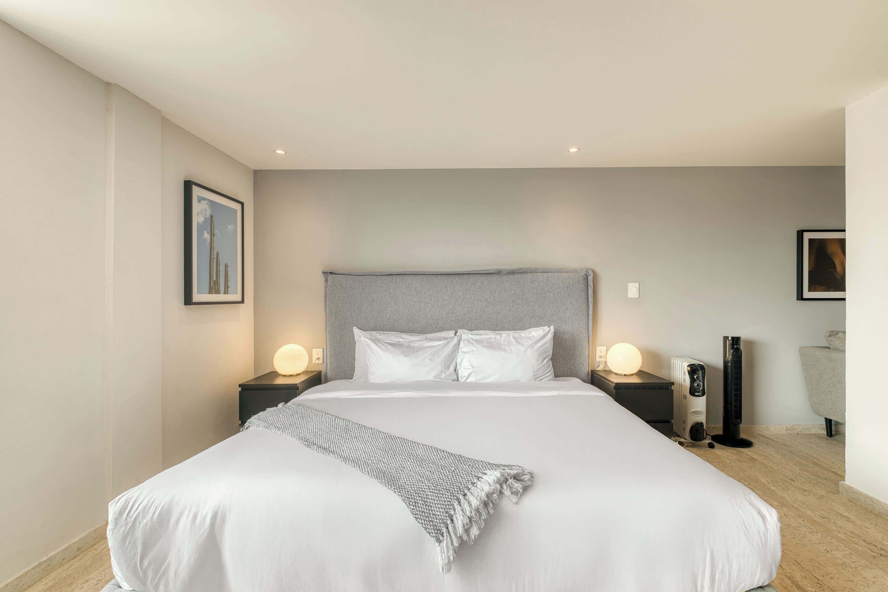 Une chambre d’hôtel moderne avec un grand lit, deux tables de chevet avec des lampes, un radiateur et une chaise.