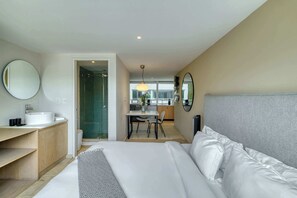 Quarto de hotel com cama, mesa de cabeceira, espelho, banheiro com pia e vista para a cidade.
