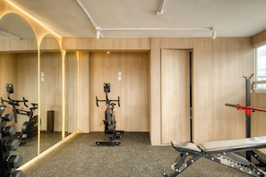 Ein Fitnessraum mit Trainingsgeräten, einer Hantelbank und einer Spiegelwand.