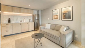 Een moderne woonkamer met een bank, een salontafel en een keukenhoek met kasten en apparatuur.