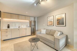 A modern living room with a sofa, a coffee table, and a kitchen area with cabinets and appliances. - Modern King Studio in Central Roma Norte (Ciudad de México)